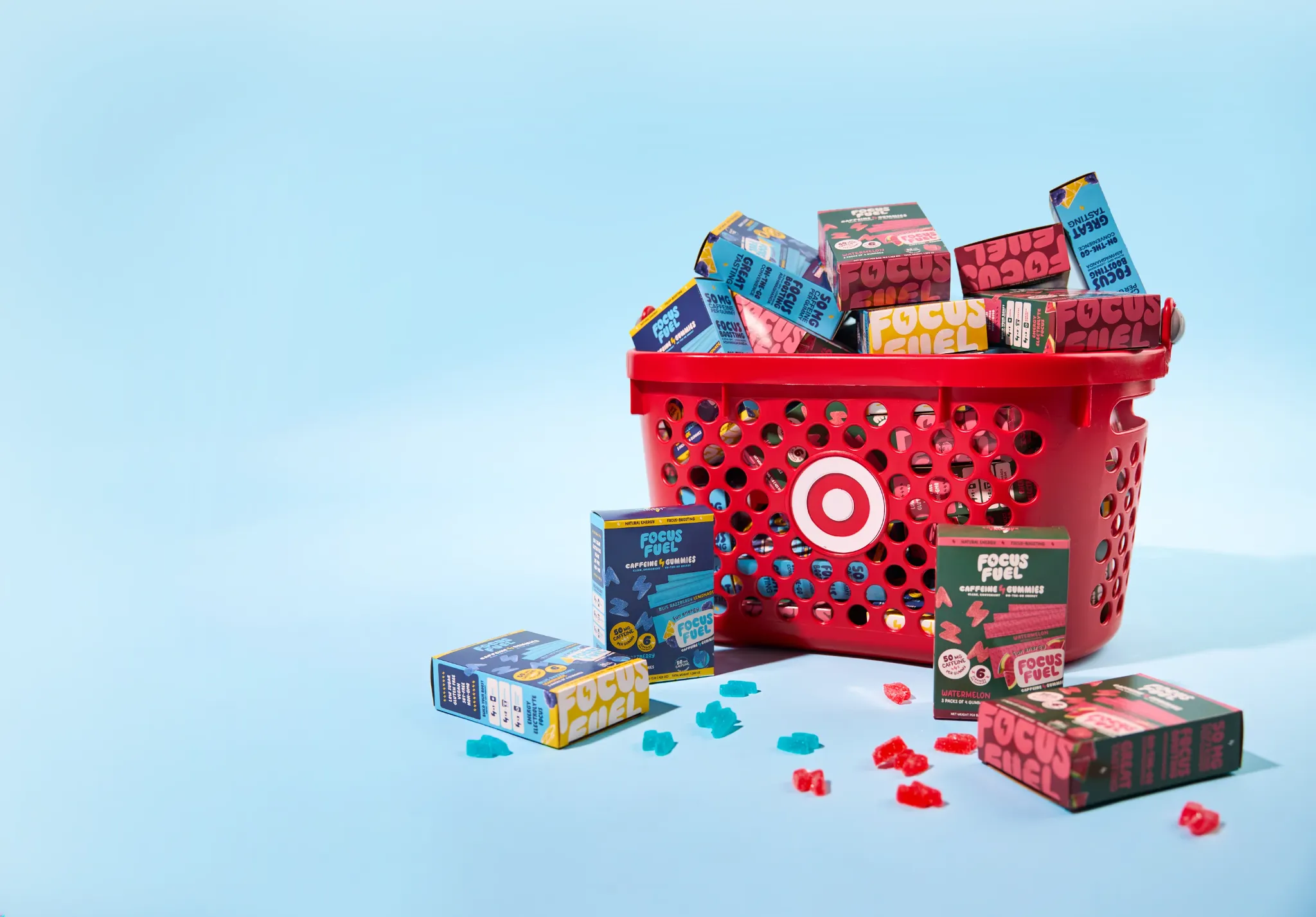 FocusFuel caffeine gummy boxes and loose gummies scattered around a red Target shopping basket overflowing with FocusFuel product on a soft light-blue backdrop.